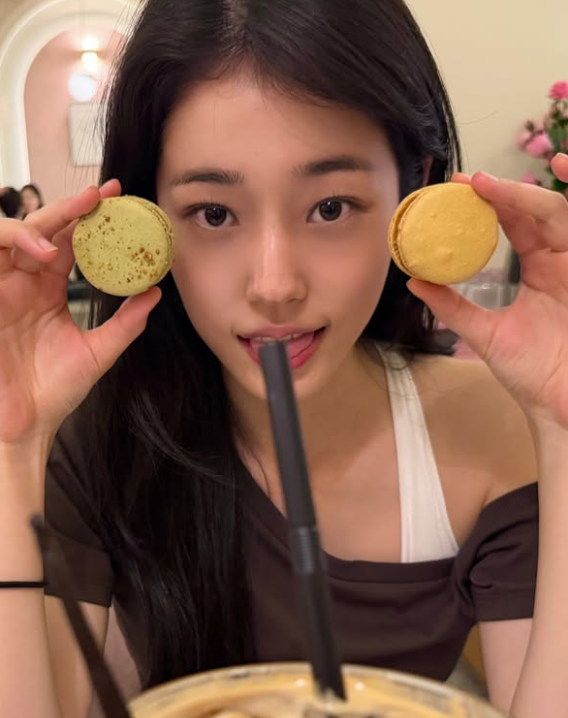Audine memegang dua macaron di dekat wajahnya